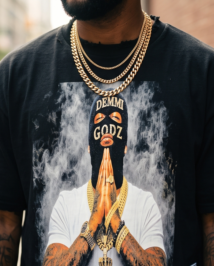 Detailed close-up of the printed Demmi Godz ski mask graphic and raw distressed collar details on a heavyweight black cotton t-shirt.